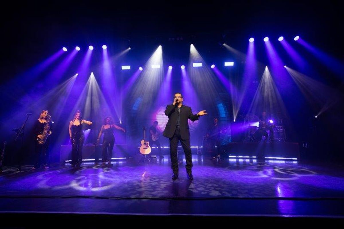 A person sings on stage with blue and white spotlights.