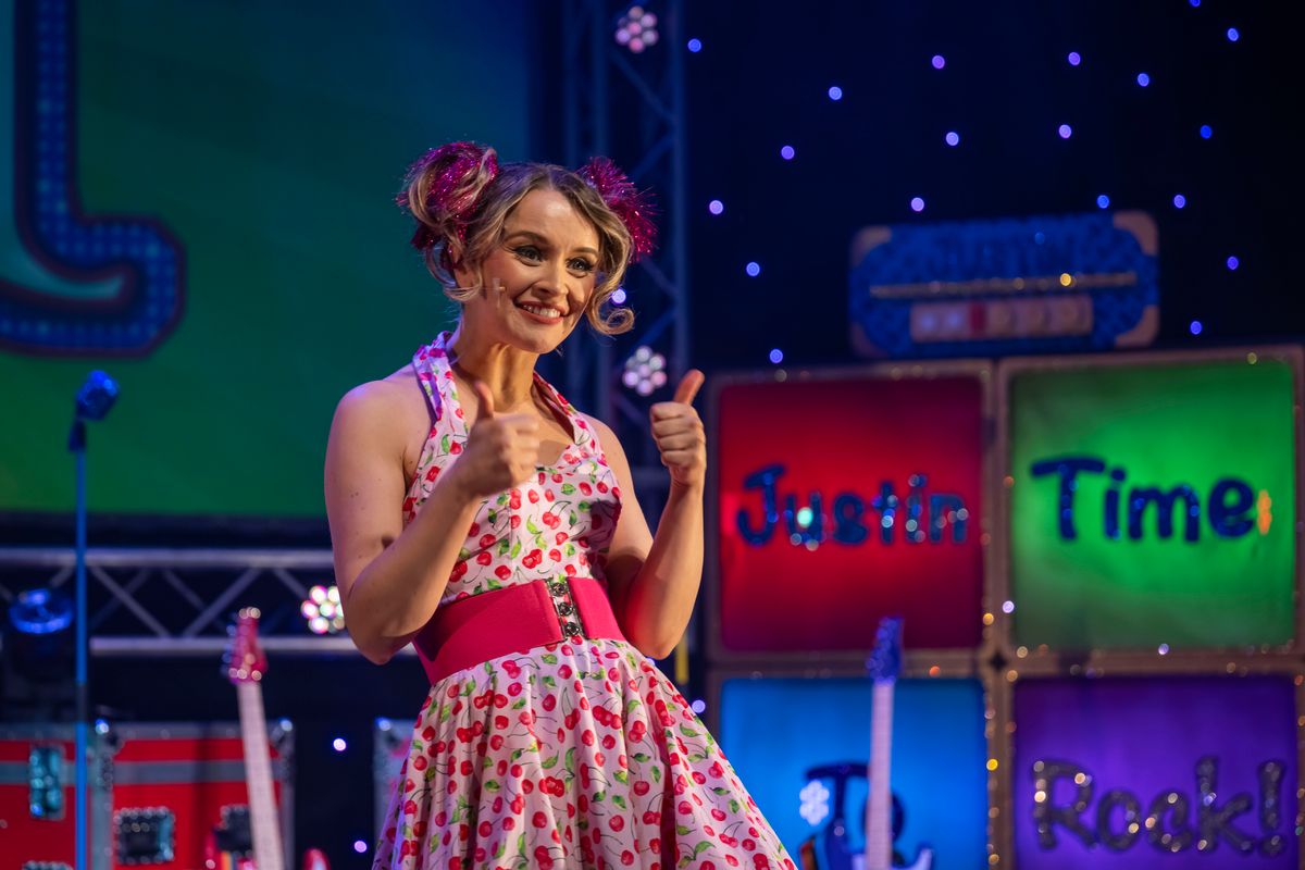 An ensemble member wearing a 1950's inspired dress and tinsel over their hair bunches gives the thumbs up to the audience.