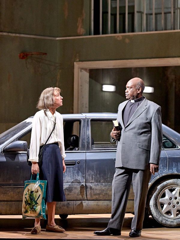 A woman and a vicar are stood beside a parked car
