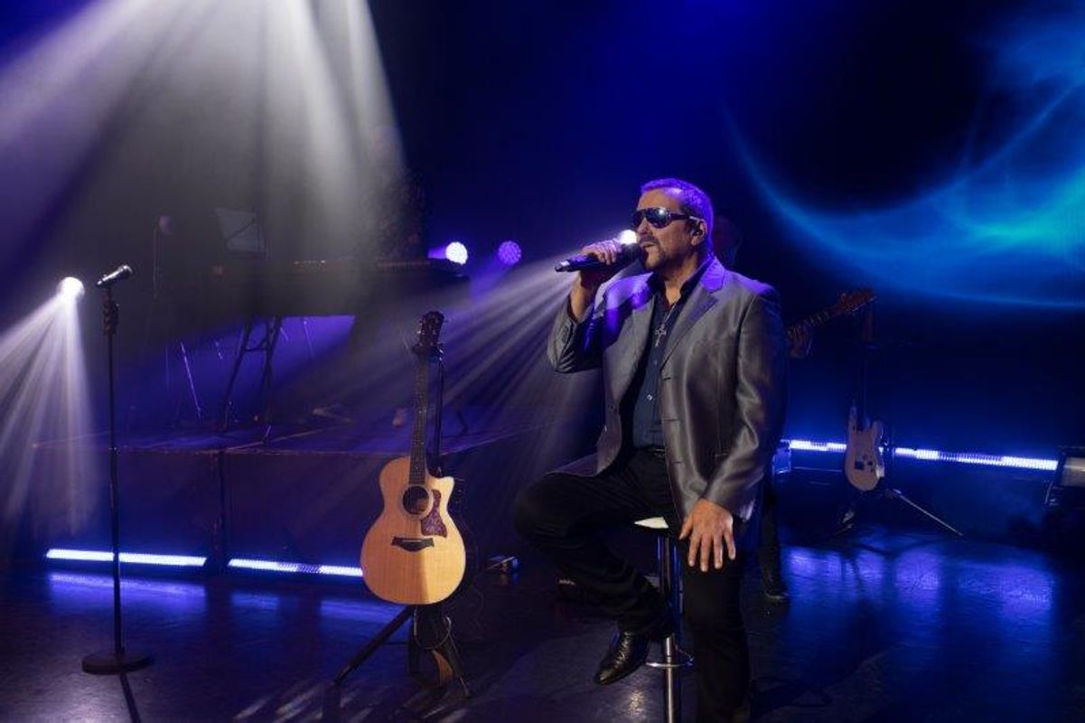 A person sits on a stool singing.