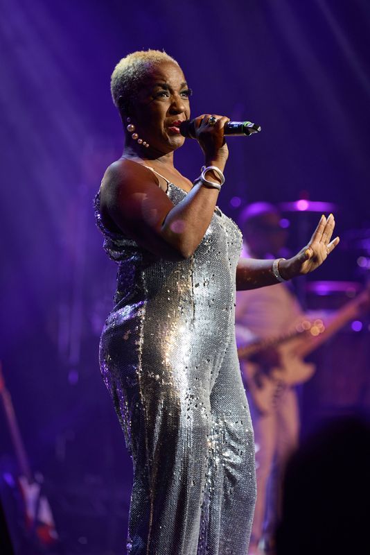 A person wearing a silver sequined jumpsuit holds a microphone.