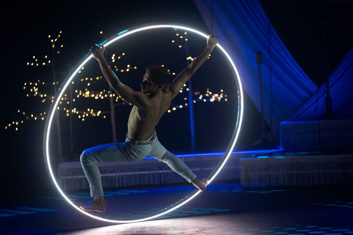 A circus performer uses a giant ring to travel around the stage.