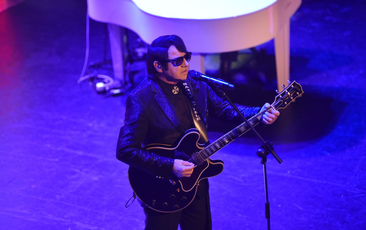 A person with a dark suit plays guitar.