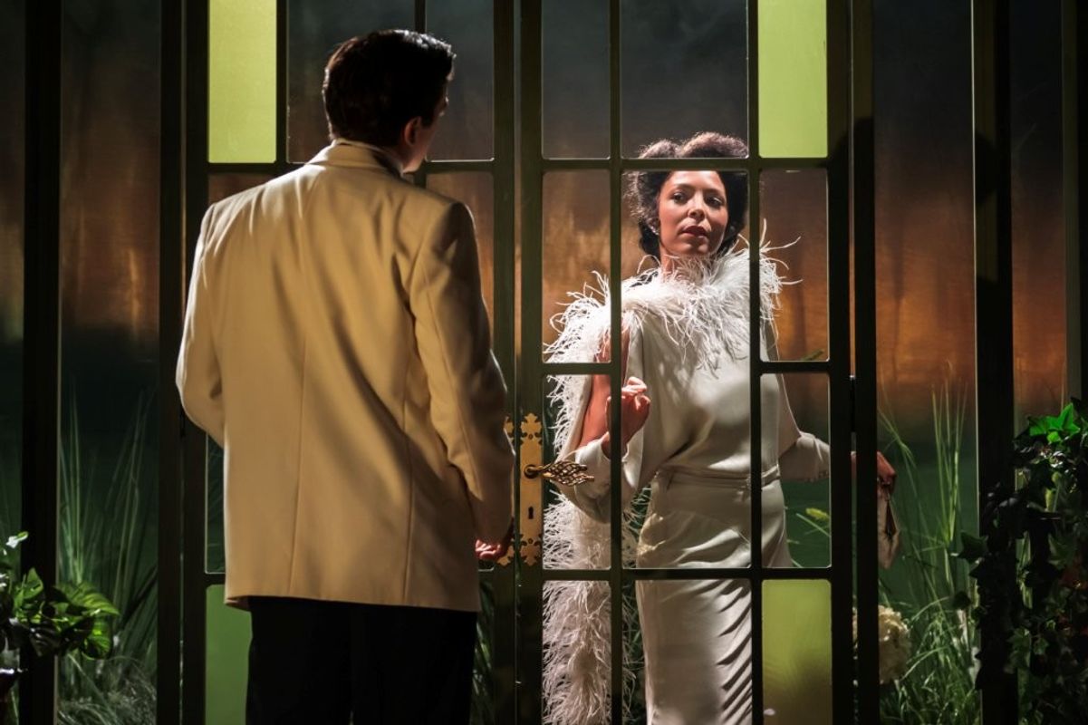 Two characters in formal evening wear standing opposite each other through a set of glass doors. They are both dressed in elegant evening wear.