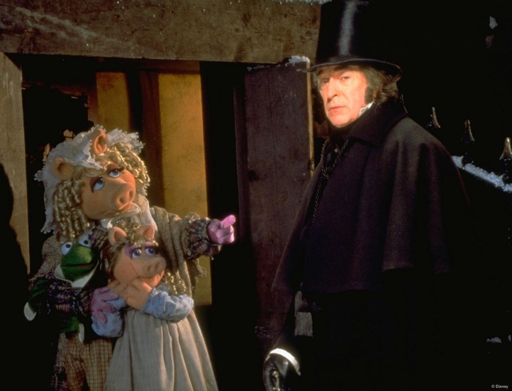 A person in a top hat and cape/coat is looking on, there are three puppets looking at him