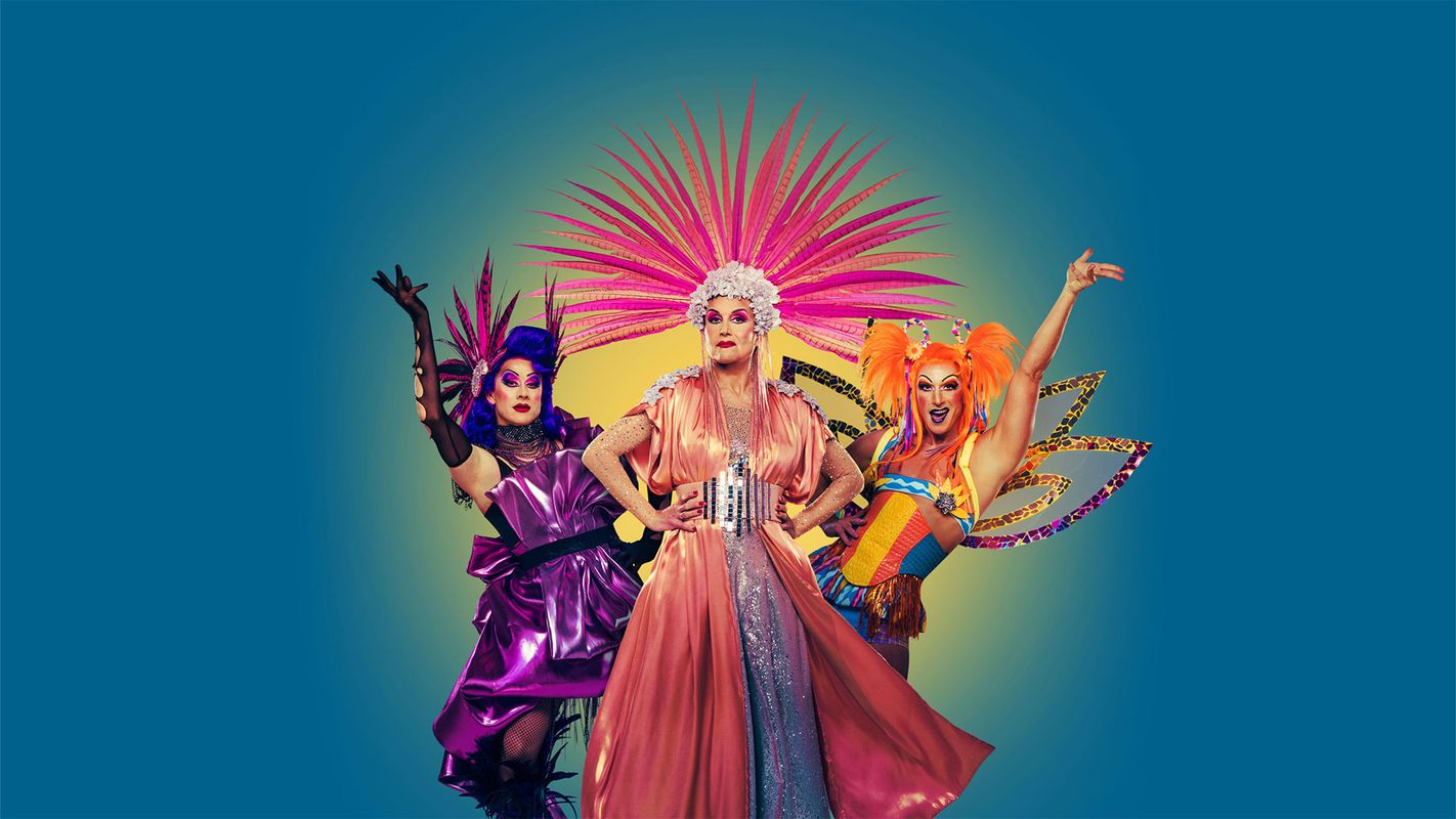 Three people pose wearing brightly coloured dresses and feathered head pieces.
