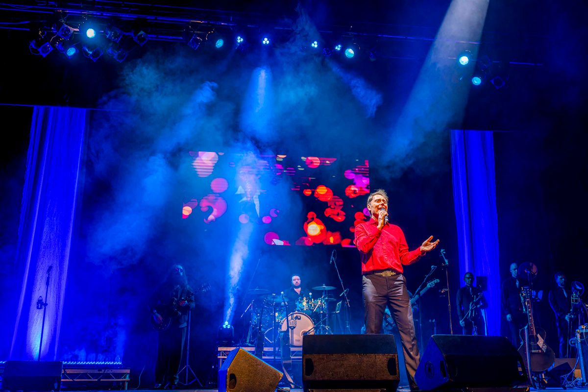 A person dressed in a red shirt sings on stage.