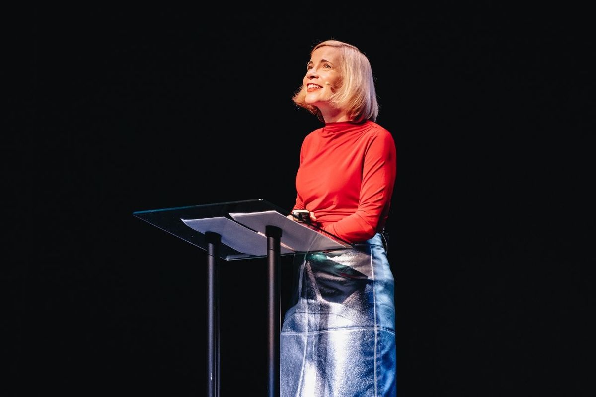 Lucy Worsley talking on stage. She is wearing a red top and a silver pencil skirt.