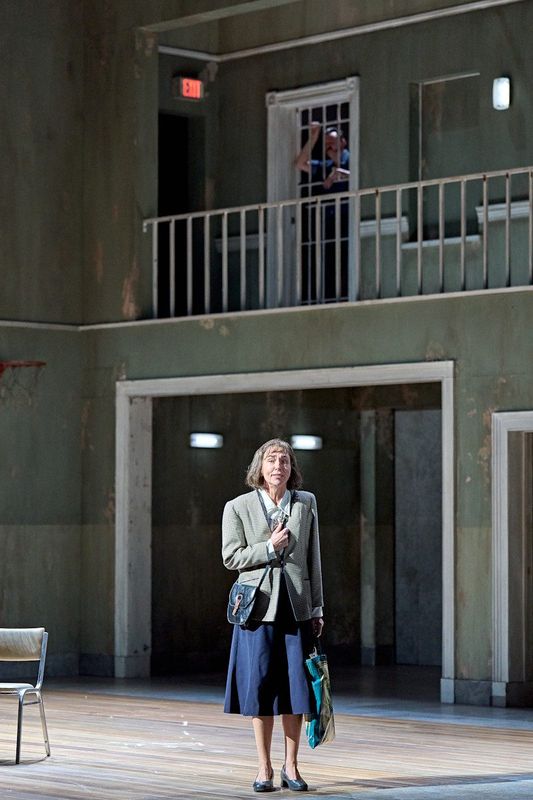 A lady is stood alone holding a bag, an inmate can be seen above in their cell