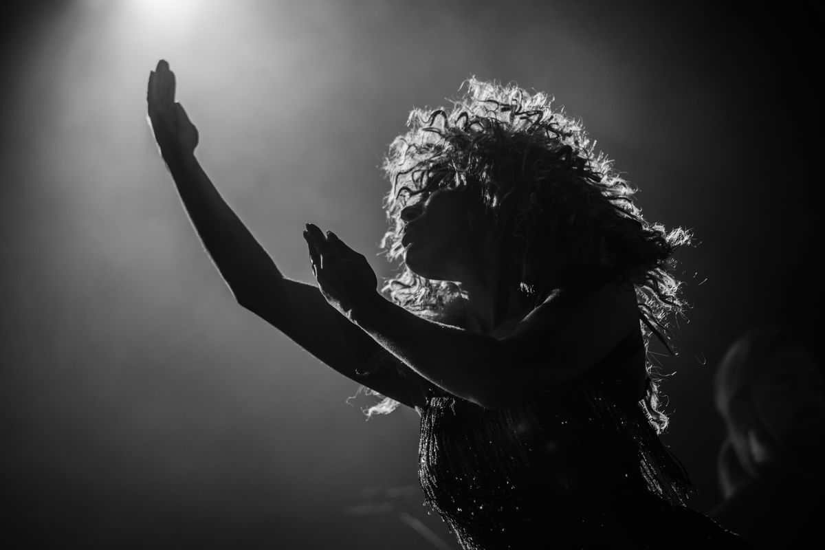 A person basks in the spotlights on stage raising both hands.