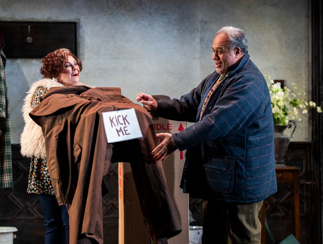 Two people, one holding up brown fabric with a sign that says kick me and the other person looking at it.