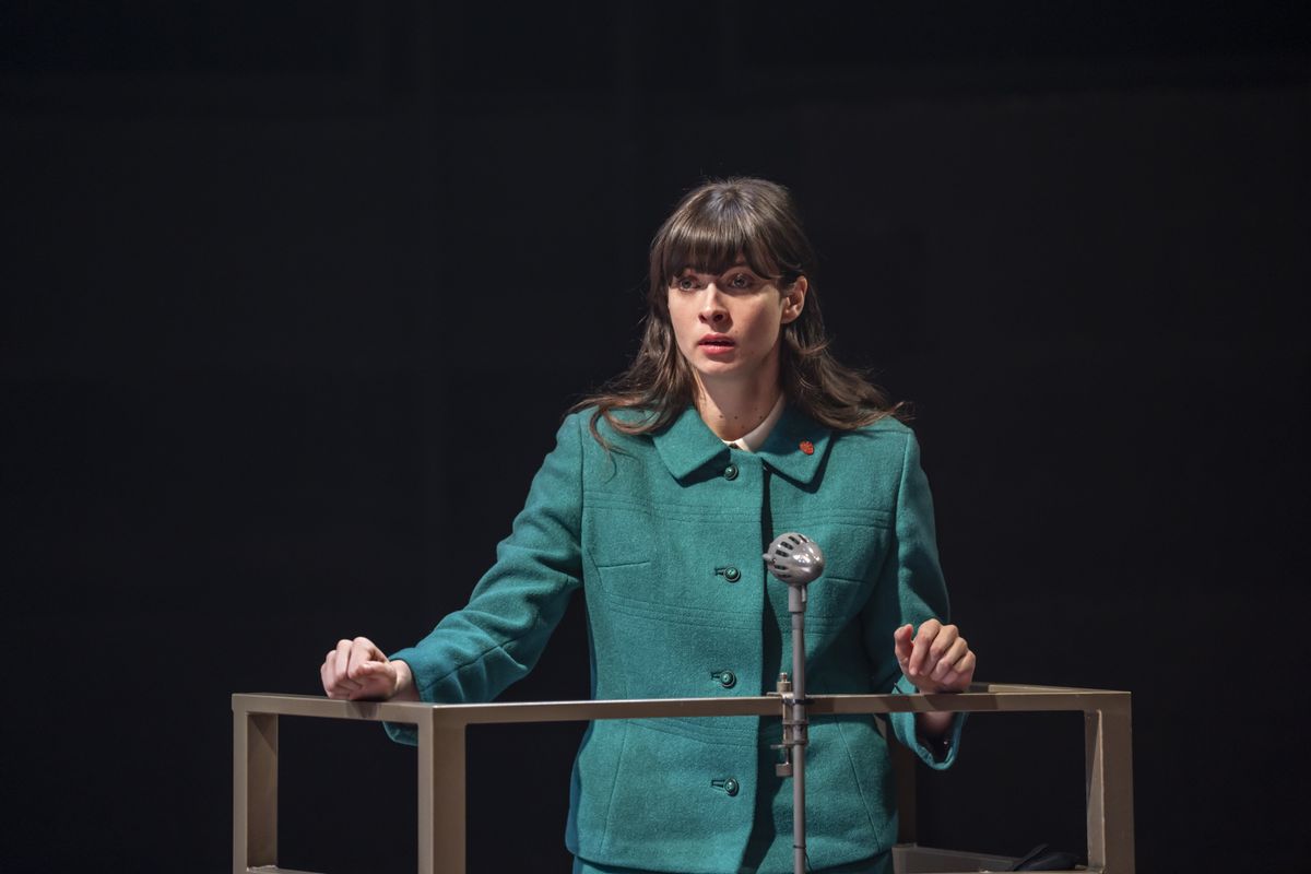 A person in a green suit stands on a platform.