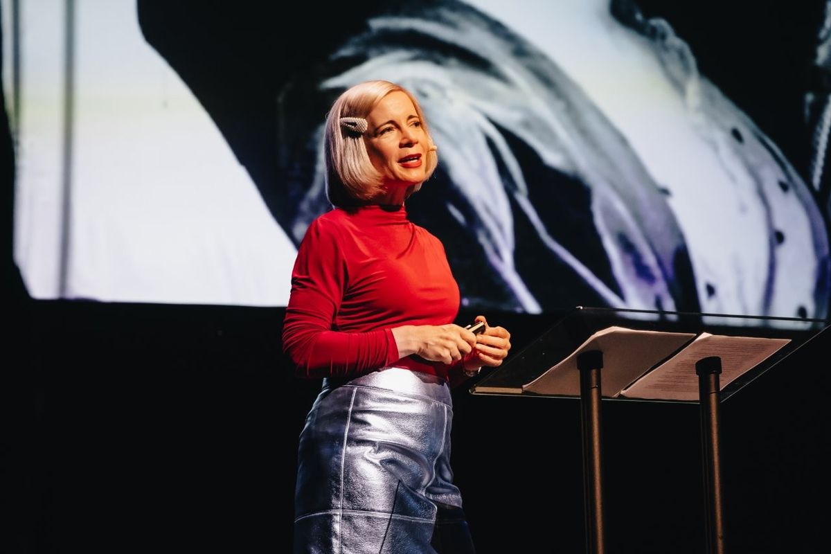 Lucy Worsley talking on stage. She is wearing a red top and a silver pencil skirt.