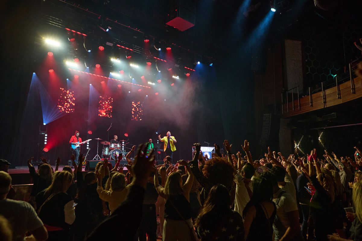 A person waring a yellow jacket encourages the audience to cheer.