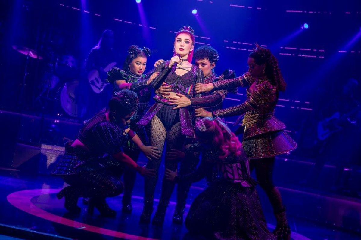 A person wearing a black and pink outfit stands centrally with five other people touching various body parts.