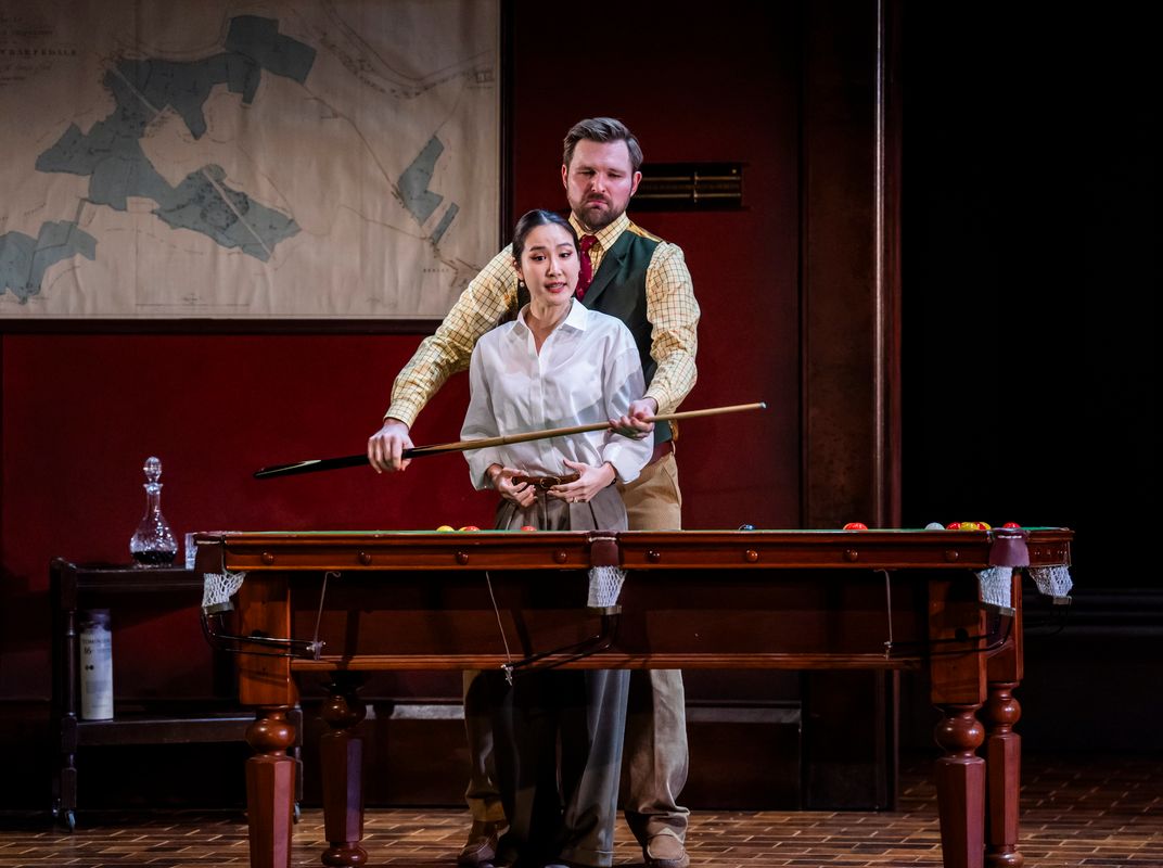Two people stood by a pool table holding a pool que