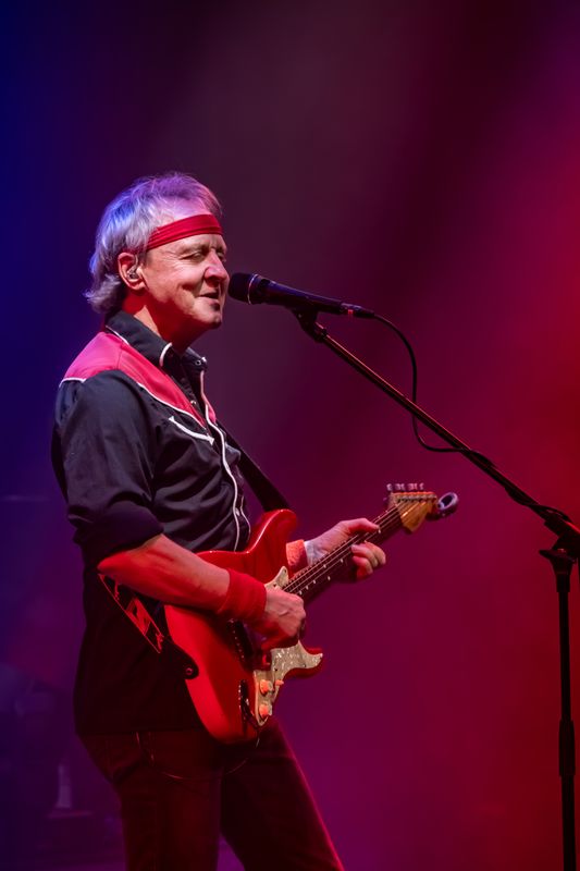 A person wearing a bandana plays a red electric guitar.