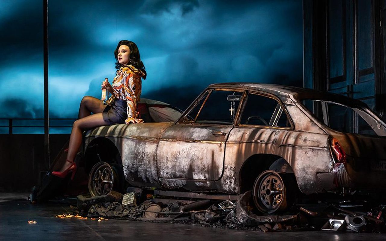 A person is sat on the bonnet of an old rusted car