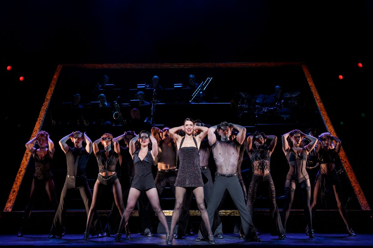 Groups of dancers in black skin tight mesh leotards and lingerie dancing on stage with low lighting