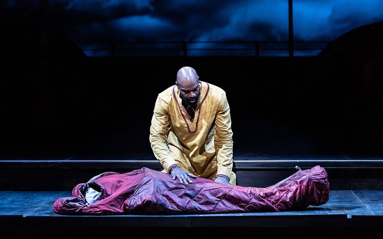 A person is kneeling beside a person who appears to be in a bodybag