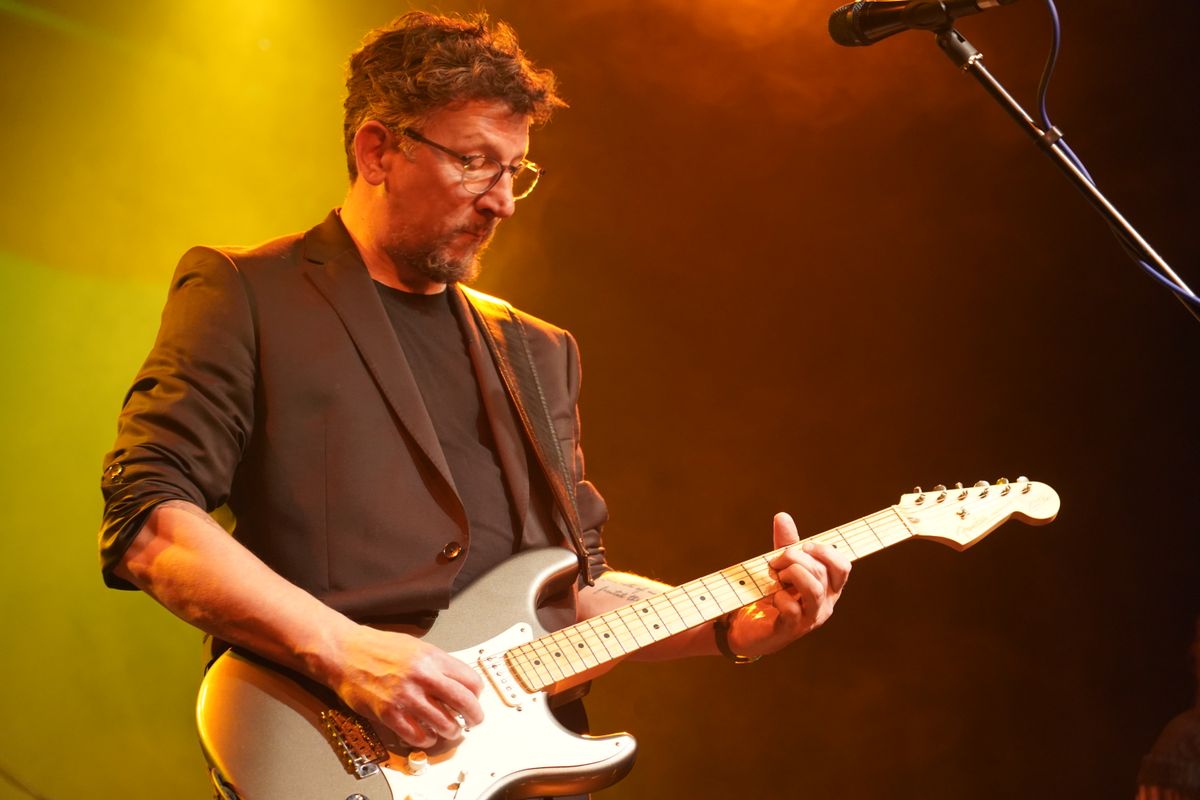 A person plays a silver electric guitar on stage.