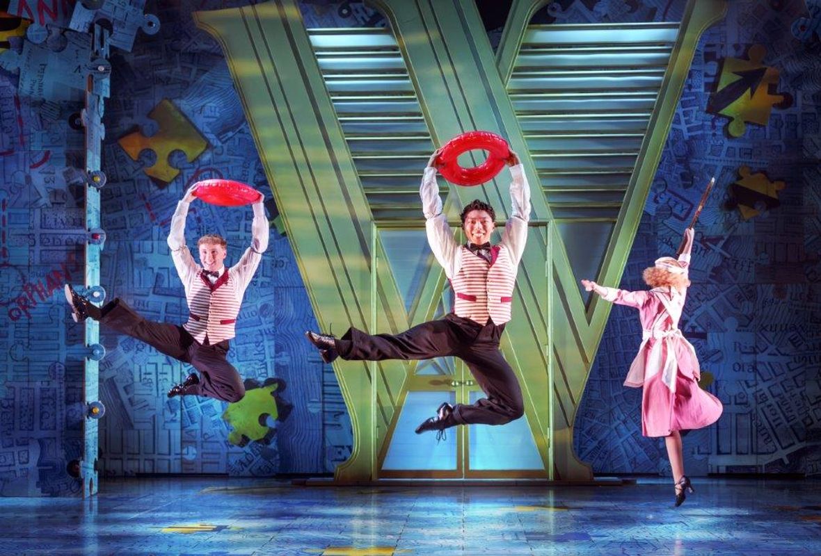 Three people in usher type clothing are jumping in the air holding inflatable red hoops