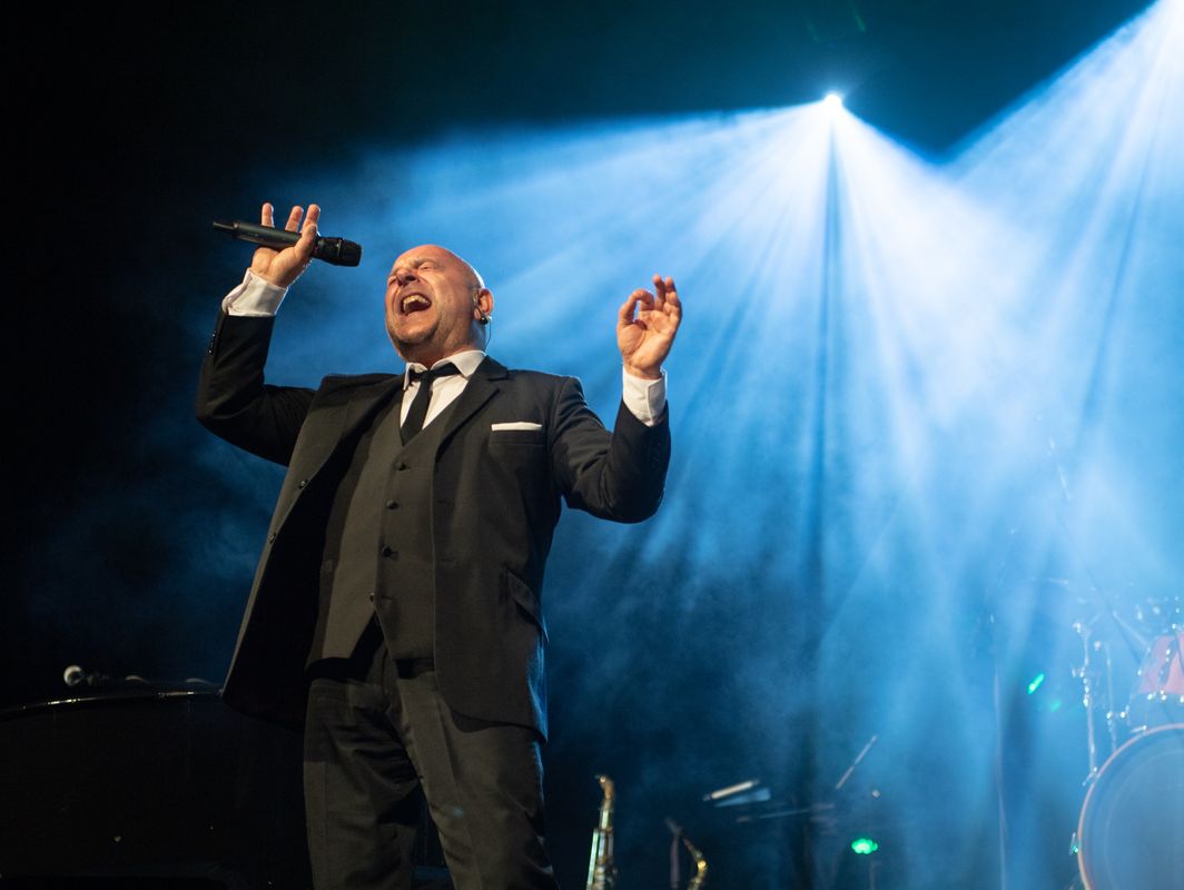 A person in a black suit sings into a microphone.