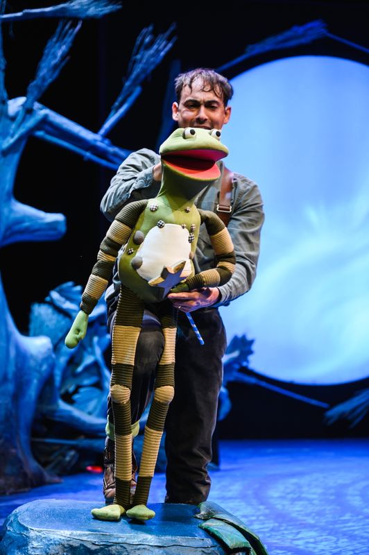 Actor holding a frog puppet onstage.