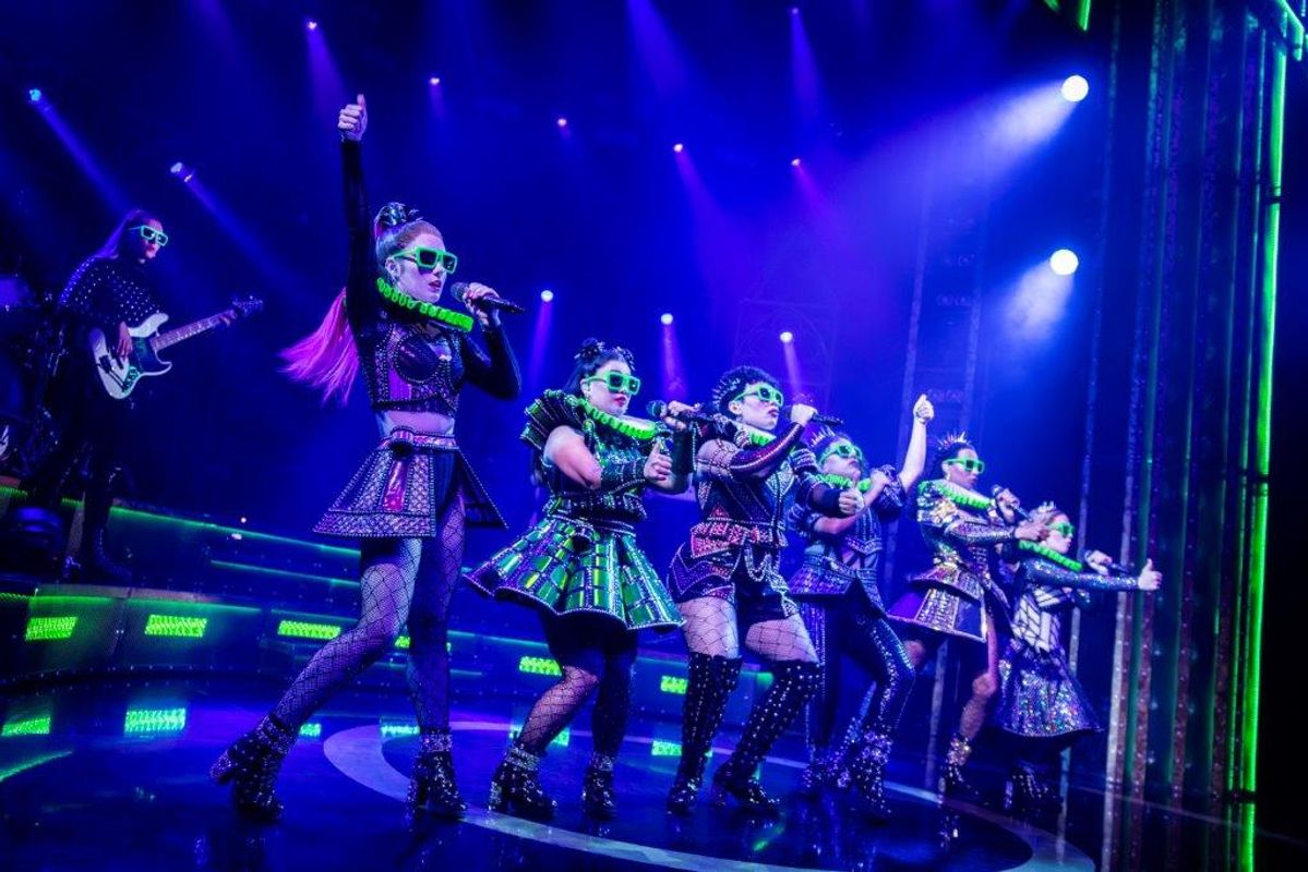 Six people stand on stage wearing neon neckpieces and glasses.