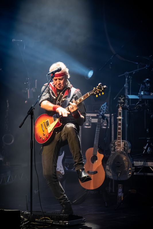 A person wearing a bandana plays an electric guitar on stage.