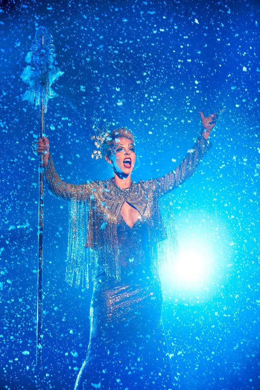 A circus performer in a bejewelled jacket is surrounded by snow.