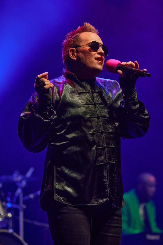 A person wearing a dark buttoned up coat sings on stage.