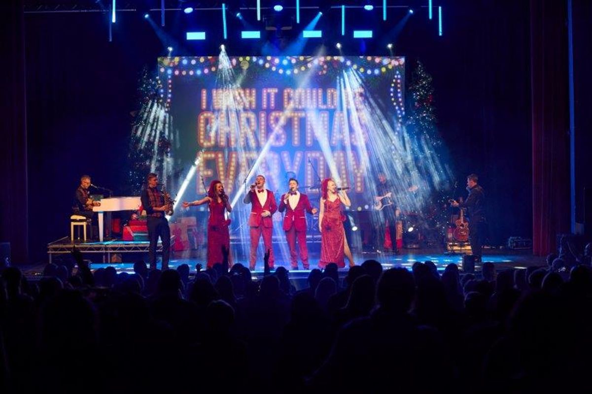 Four people dressed in red are centre stage with musicians surrounding them. 