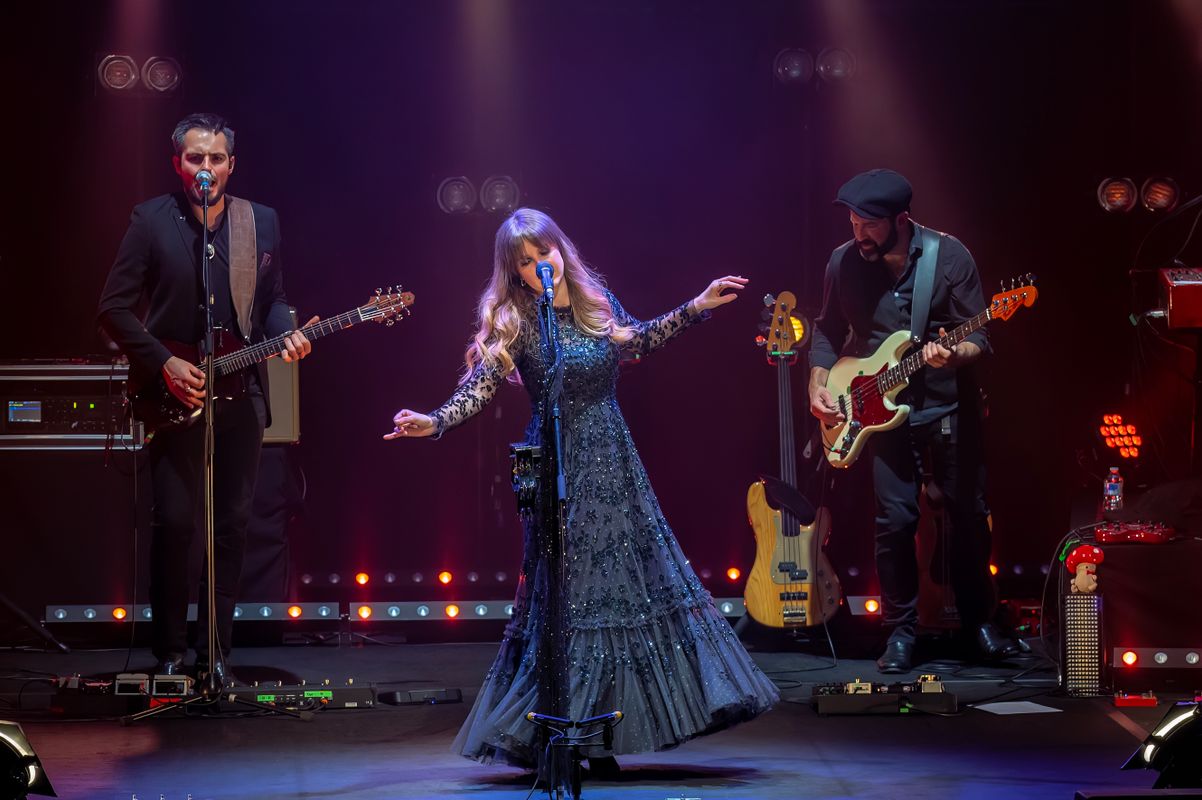 A person in a lacey black dress sings on stage.
