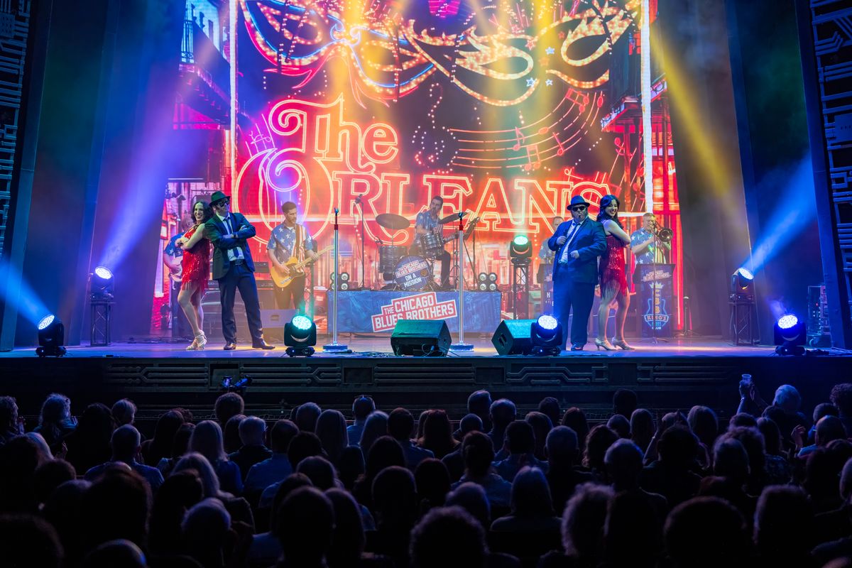 Two people dressed in suits are accompanied by two dancers on stage.