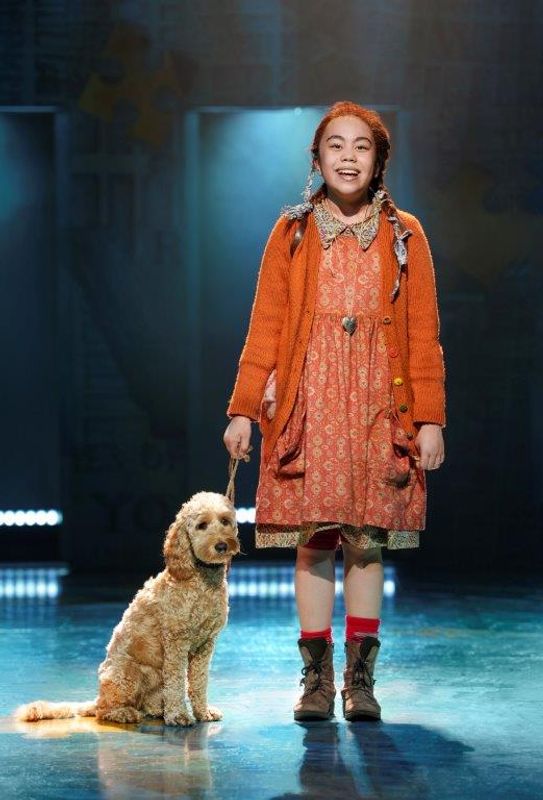 A young girls wearing orange and has a little dog beside her