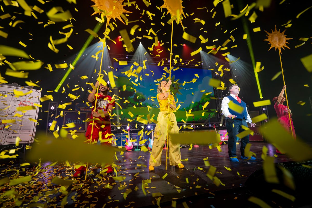 The company stand holding giant  yellow sticks and  are surrounded by falling yellow confetti.