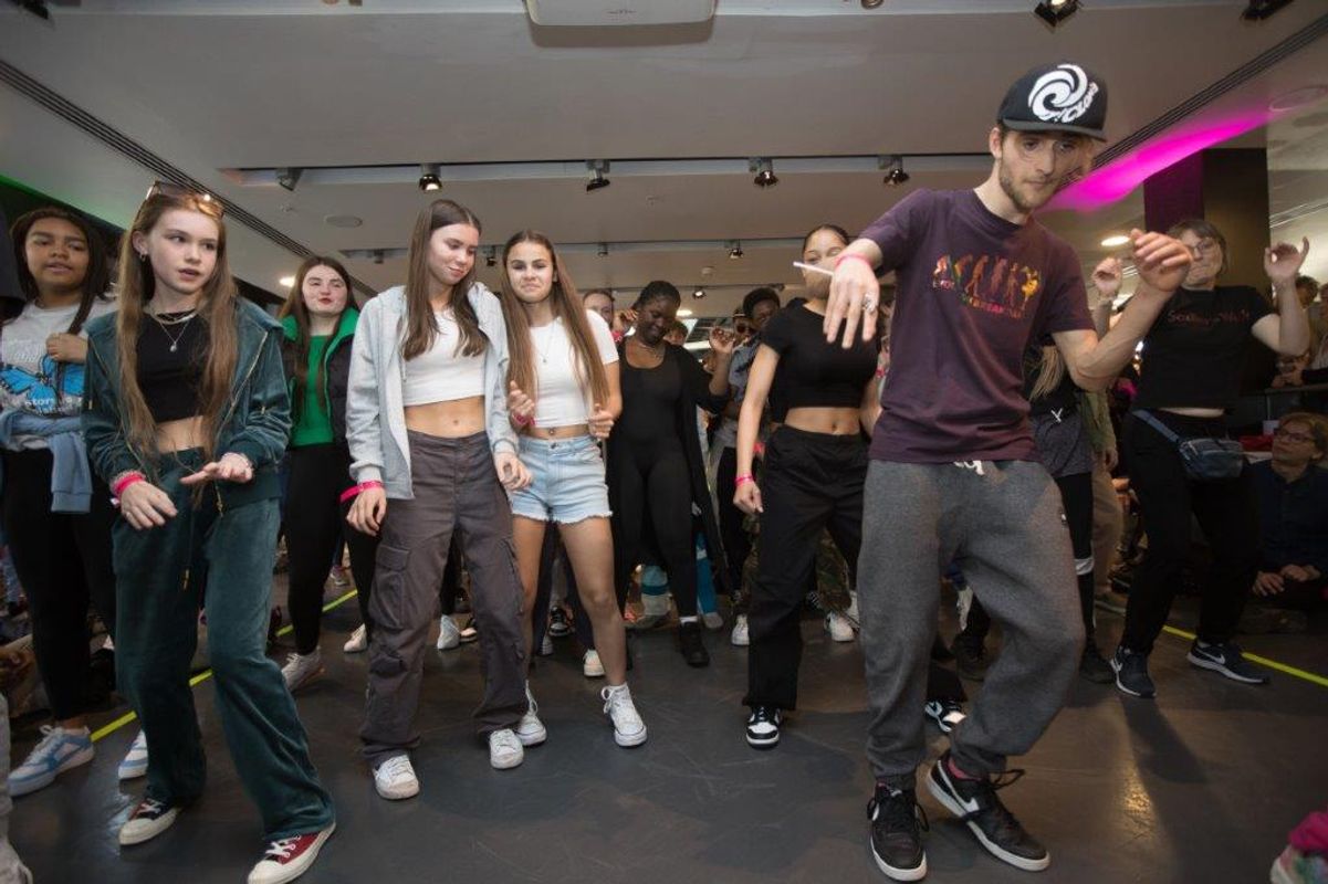 A person breakdances whilst a group of young people try and emulate.