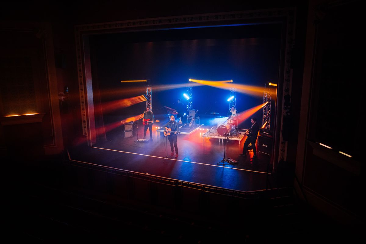 Three guitarists play on stage surrounded by orange lights.