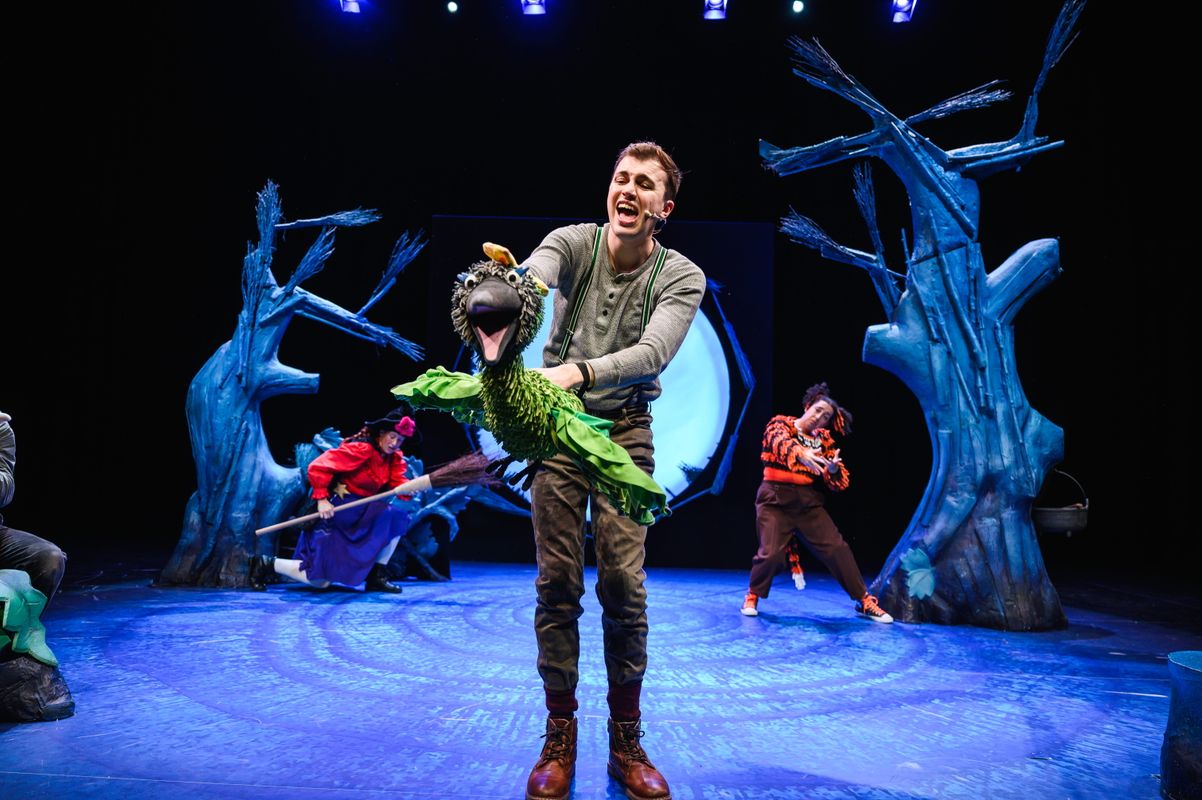 Actor holding a bird puppet onstage.