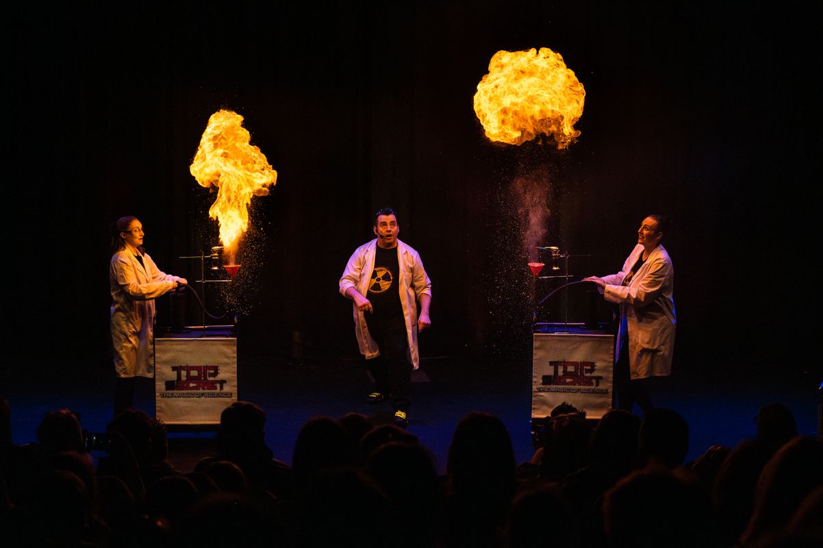 3 people stand on stage looking at two fireballs.