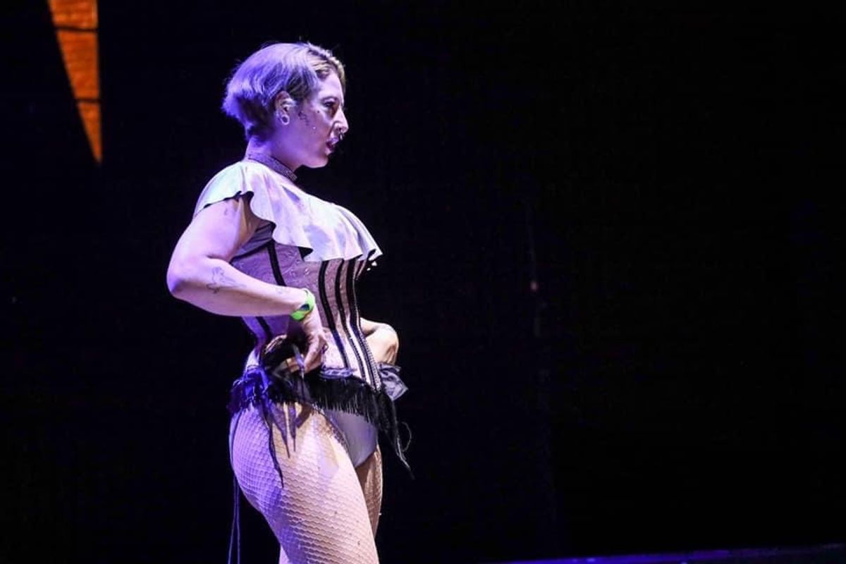 Person stood on stage, purple lighting, they are wearing a corset and fishnet tights