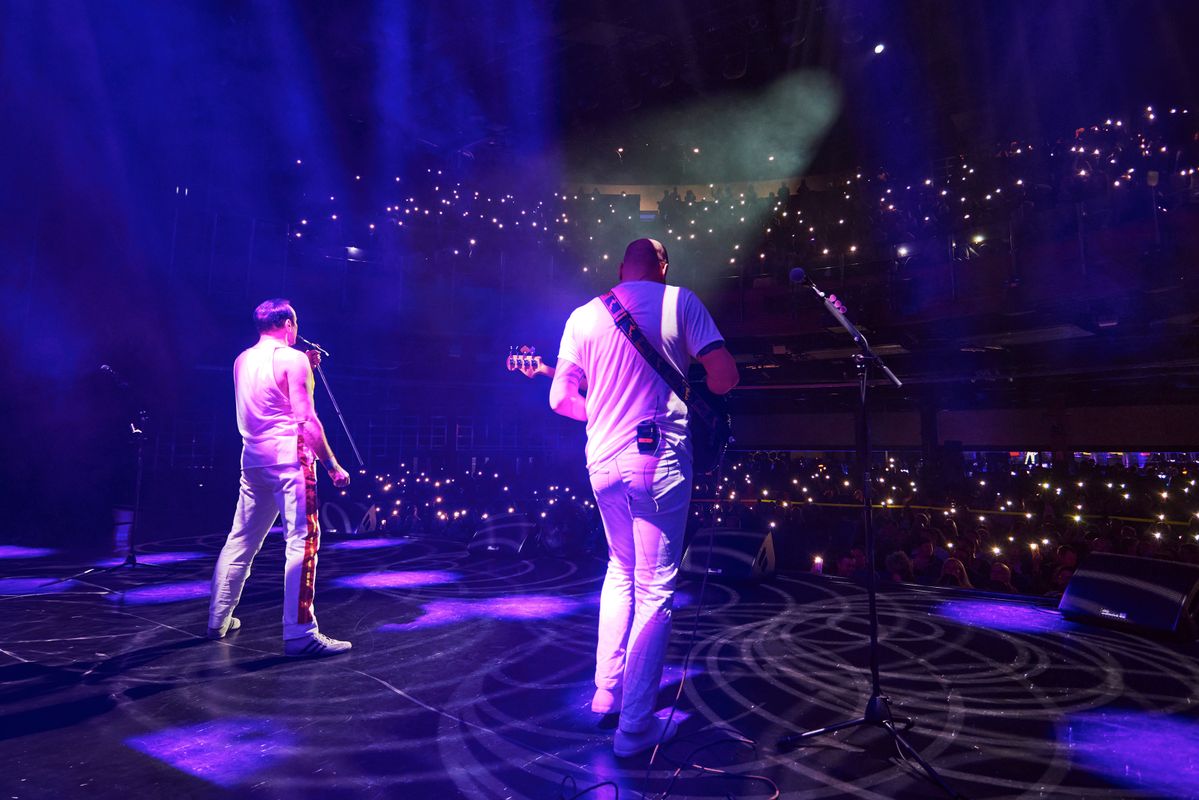 Performers singing and playing instruments on stage to an audience, bright lights are shining on the band