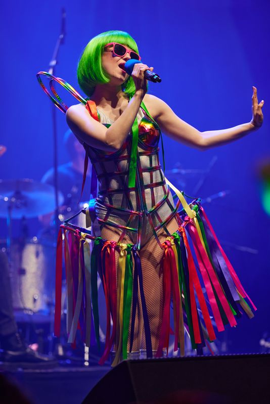 A person wearing a bright green wig sings on stage.