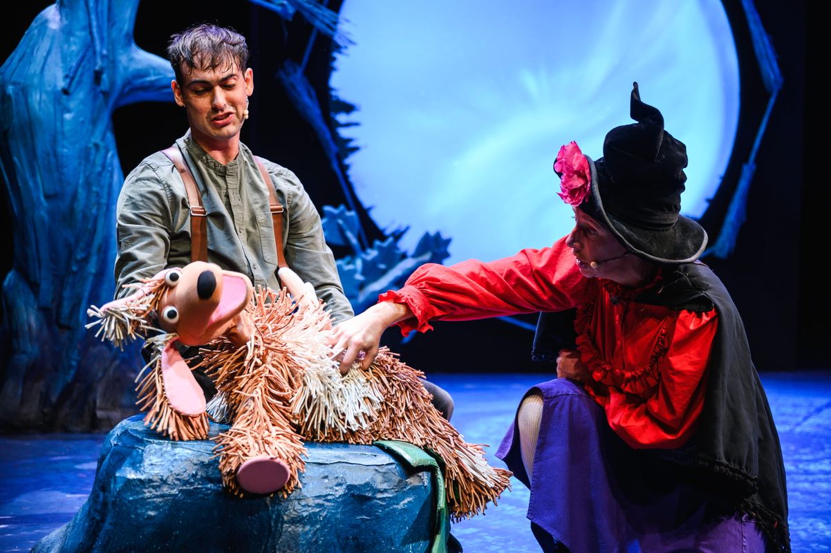 Two actors with a dog puppet onstage.