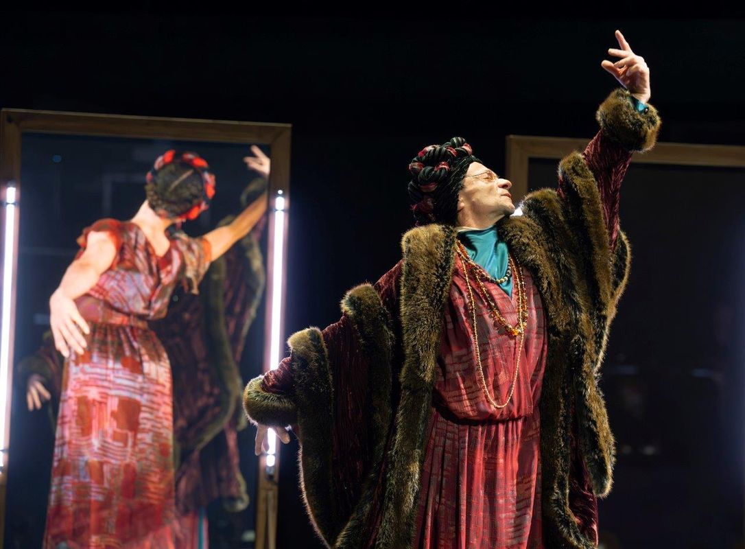 Two dancer are performing back to back, one is wearing a large fur coat