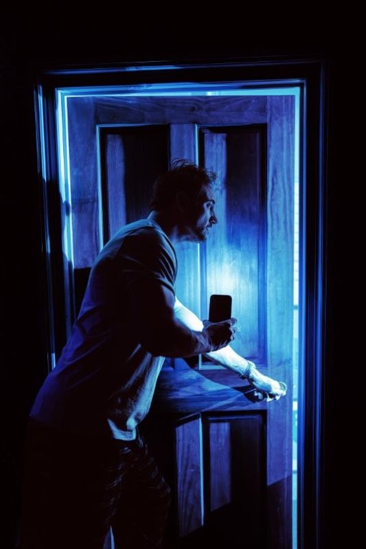 A silhouette of a person holding a flashlight, cautiously opening a door in a dark room. The scene conveys suspense and mystery.