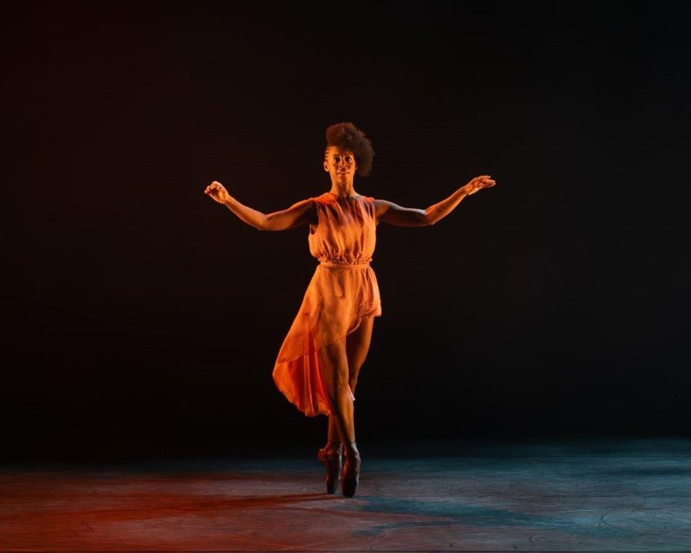 Dancer on stage with her arms out slightly as she stands on her tip toes