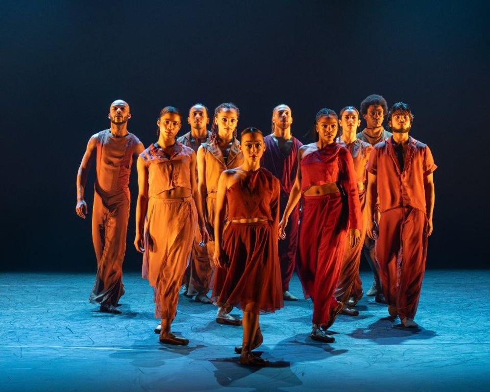 Group of dancers in orange and brown clothing with a soft spot light on them