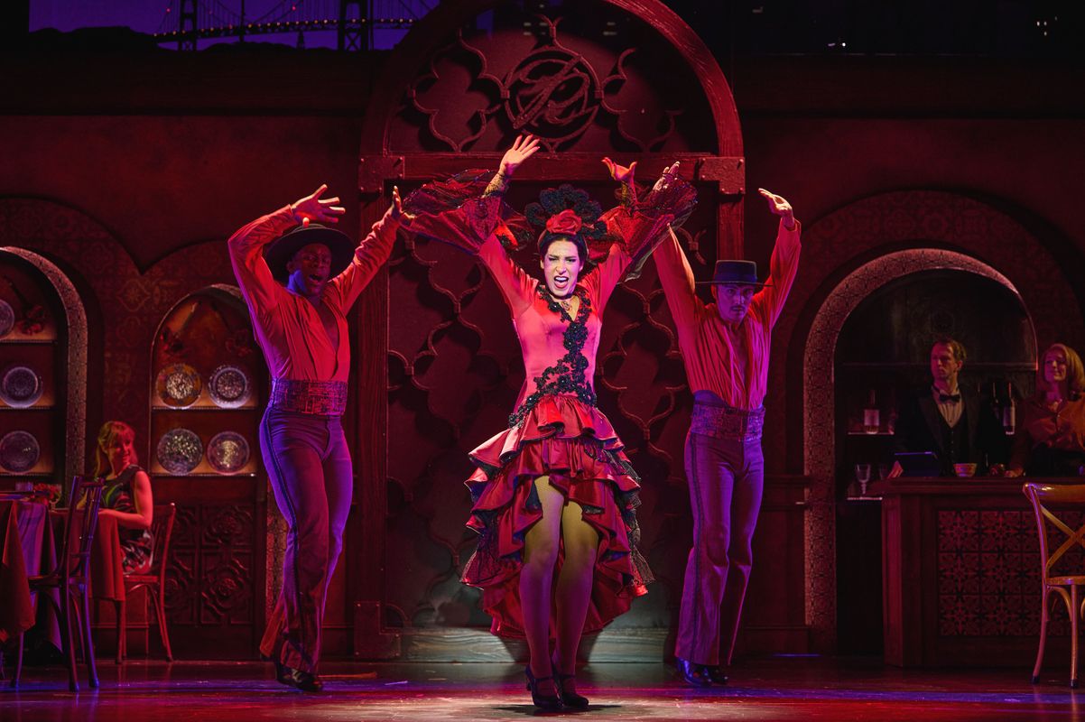 A female dances flamenco in a bright red ruffled costume with dancers either side.